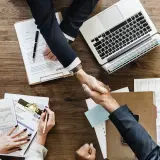 Accordo raggiunto: stretta di mano tra due uomini d'affari, con laptop e documenti. Il contraente significato è chiaro: un patto siglato.