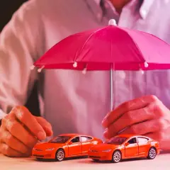 Due macchinine arancioni sotto un ombrello rosa. La protezione è importante, esiste ancora la legge Bersani per assicurare i veicoli.
