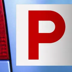 Targa "P" rossa su sfondo bianco, applicata su un'auto blu. Indica un neopatentato alla guida.