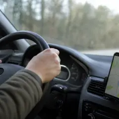 Mani sul volante, un cellulare con mappa mostra la strada. La guida con cellulare è essenziale per orientarsi.
