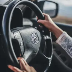 Mani sul volante di una Toyota, con un braccio che indossa una maglia decorata. Finalmente posso guidare una macchina non intestata a me, verso l'avventura.