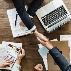 Accordo raggiunto: stretta di mano tra due uomini d'affari, con laptop e documenti. Il contraente significato è chiaro: un patto siglato.