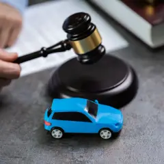 Martelletto da giudice vicino a un'auto blu giocattolo, suggerisce il costo della perdita di possesso in un contesto legale.