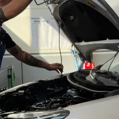 Meccanico con tatuaggi controlla il motore, parte essenziale del tagliando della macchina.