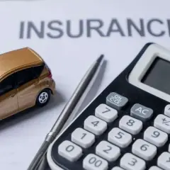 Modellino auto dorata su foglio "INSURANCE", calcolatrice e penna. L'auto intestata al figlio, l'assicurazione al padre.