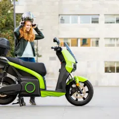 Donna sorridente mette il casco accanto al suo scooter elettrico verde brillante.