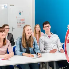 Insegnante mostra un segnale stradale a studenti sorridenti. Si può guidare di notte con il foglio rosa A1?