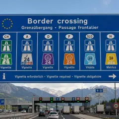 Cartello stradale indica "Border crossing" con simboli per vignetta autostradale. In Slovenia serve la vignetta, come indicato da "SLO" e "Vinjeta".