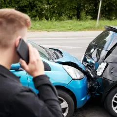 Uomo al telefono dopo un incidente. Le auto sono danneggiate, un sinistro che richiederà un **scoperto assicurativo**.