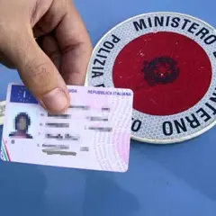 Patente italiana in mano, accanto a un disco di Polizia Stradale. Guida sicura per sapere come recuperare i punti della patente.