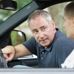 Un istruttore spiega a un giovane dove può guidare con il foglio rosa, indicando il volante.