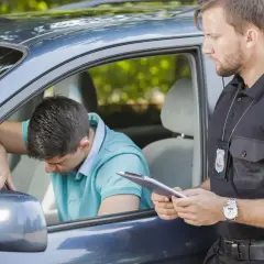 Agente di polizia parla con un automobilista, forse per evitare sospensione patente pagando una multa.