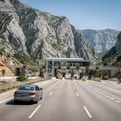 Un'auto attraversa un casello autostradale tra montagne rocciose. Calcolare quanto costa andare in Croazia in macchina è fondamentale per pianificare il viaggio.