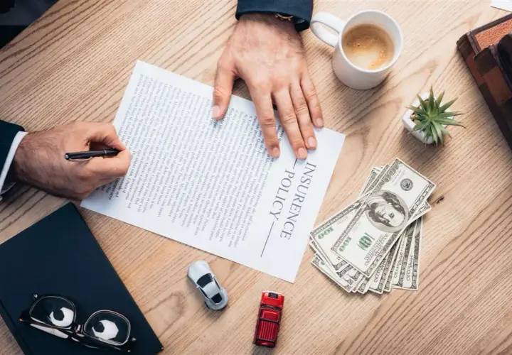 Firma un contratto di assicurazione senza franchigia: cosa significa? Pagamento in contanti, auto e caffè sul tavolo.