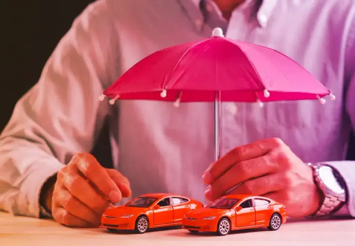 Due macchinine arancioni sotto un ombrello rosa. La protezione è importante, esiste ancora la legge Bersani per assicurare i veicoli.