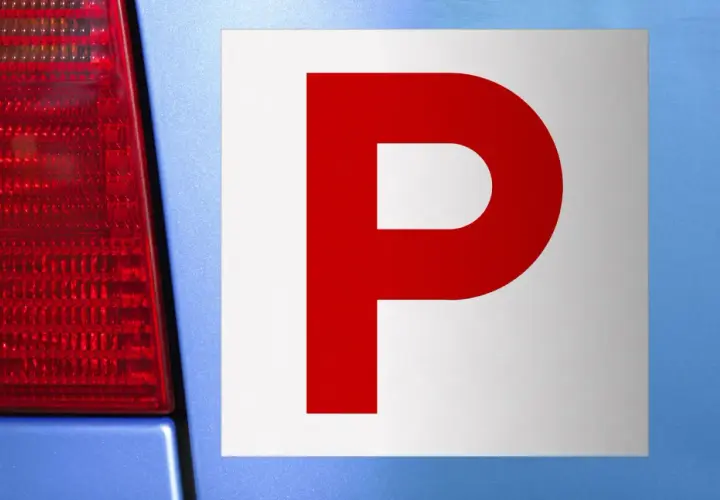 Targa "P" rossa su sfondo bianco, applicata su un'auto blu. Indica un neopatentato alla guida.