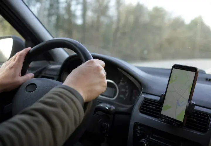 Mani sul volante, un cellulare con mappa mostra la strada. La guida con cellulare è essenziale per orientarsi.