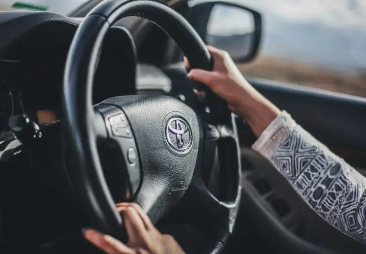 Mani sul volante di una Toyota, con un braccio che indossa una maglia decorata. Finalmente posso guidare una macchina non intestata a me, verso l'avventura.