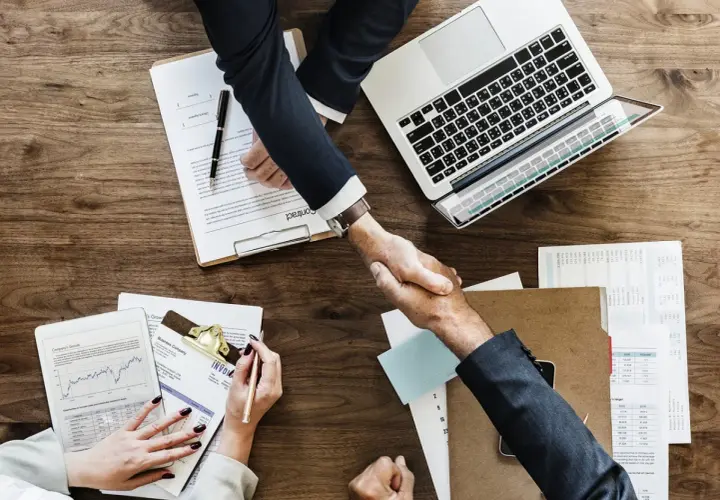 Accordo raggiunto: stretta di mano tra due uomini d'affari, con laptop e documenti. Il contraente significato è chiaro: un patto siglato.