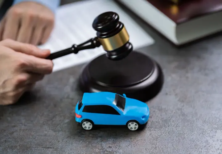 Martelletto da giudice vicino a un'auto blu giocattolo, suggerisce il costo della perdita di possesso in un contesto legale.