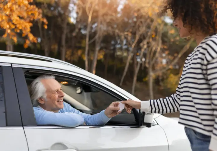 Un uomo anziano in auto sorride mentre riceve documenti per rinnovo patente dopo 70 anni da una giovane donna.