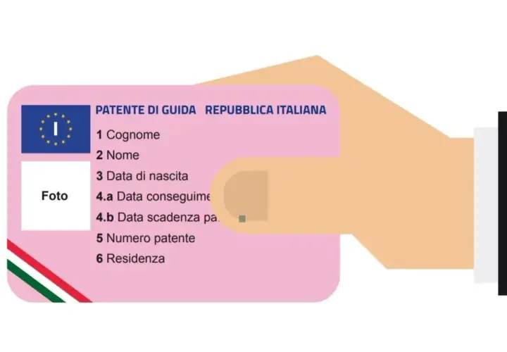 Una mano tiene una patente di guida italiana, un documento essenziale per la circolazione, che a volte non è duplicabile.