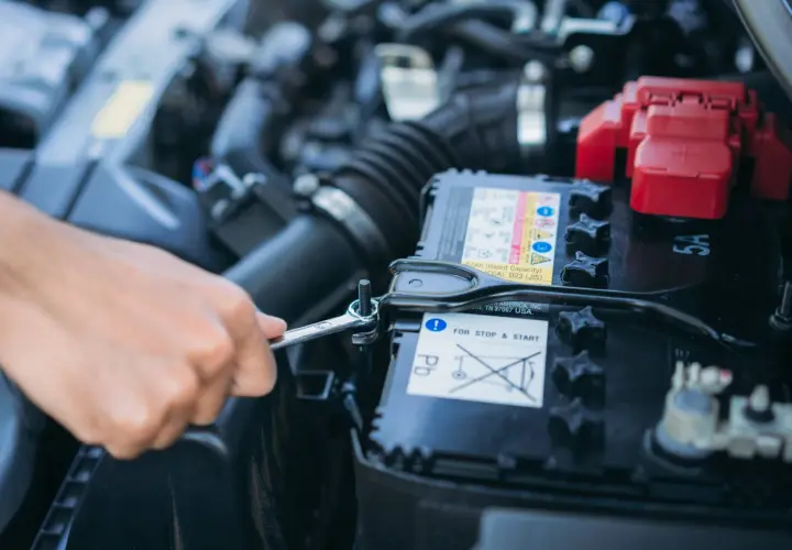 Mano con chiave inglese che allenta il bullone per staccare la batteria auto e non farla scaricare.