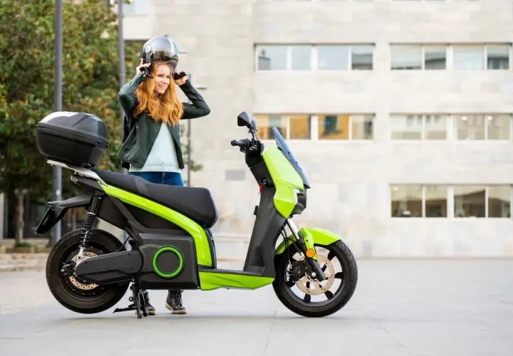 Donna sorridente mette il casco accanto al suo scooter elettrico verde brillante.