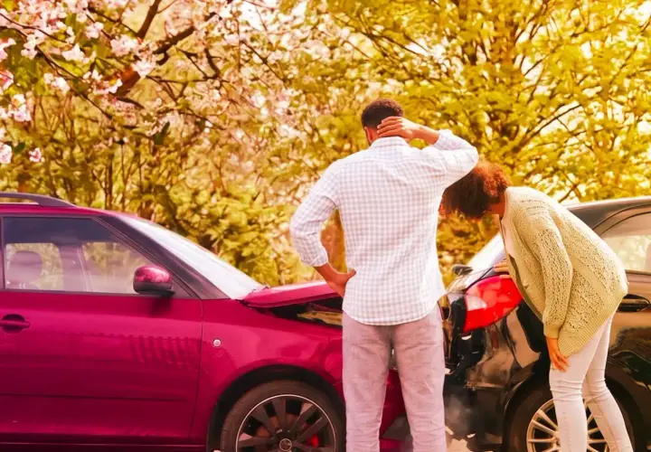 Coppia esamina i danni dopo un incidente. Il cofano di un'auto rossa è aperto, mentre un'altra auto nera è danneggiata. Il **RCA significato** è la copertura assicurativa obbligatoria.