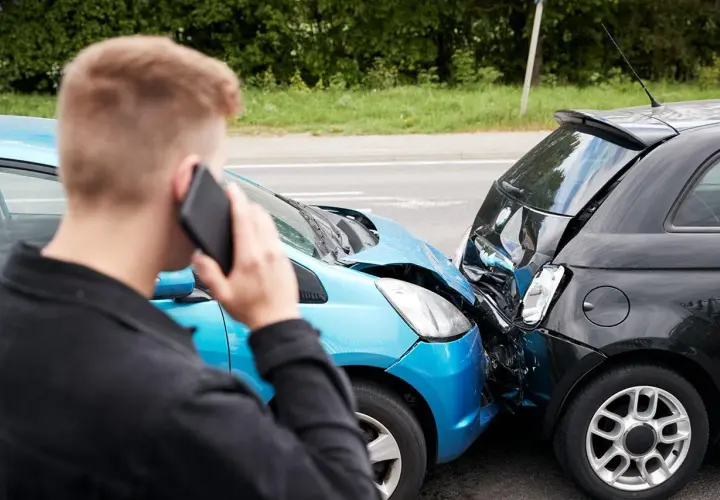 Uomo al telefono dopo un incidente. Le auto sono danneggiate, un sinistro che richiederà un **scoperto assicurativo**.