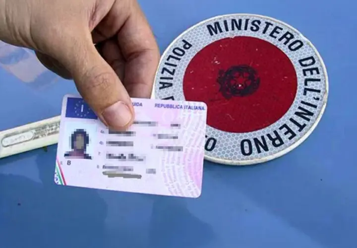 Patente italiana in mano, accanto a un disco di Polizia Stradale. Guida sicura per sapere come recuperare i punti della patente.