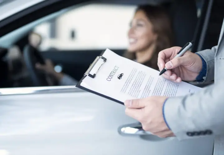 Uomo in giacca firma un contratto d'assicurazione auto. La donna al volante sorride. La decorrenza assicurazione è un dettaglio importante.