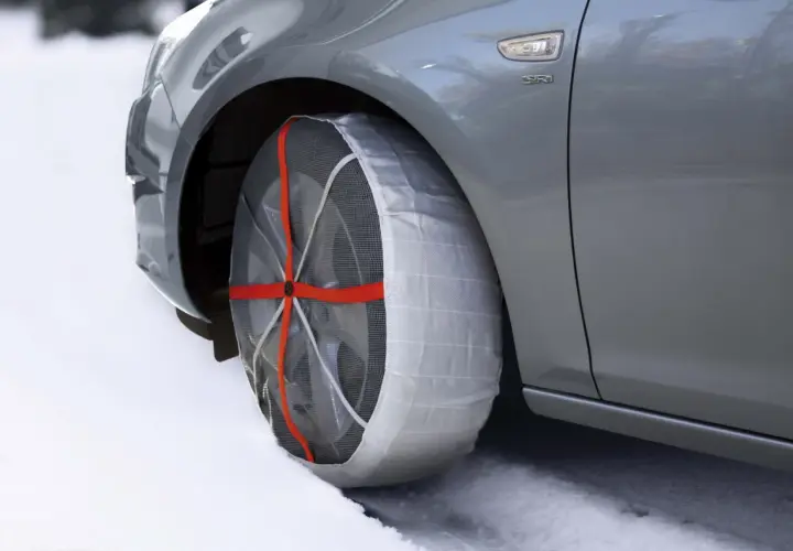 Auto grigia su neve con calze da neve omologate montate su una ruota. Sicurezza invernale garantita.