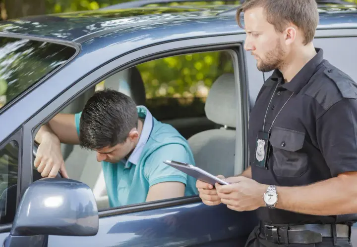 Agente di polizia parla con un automobilista, forse per evitare sospensione patente pagando una multa.