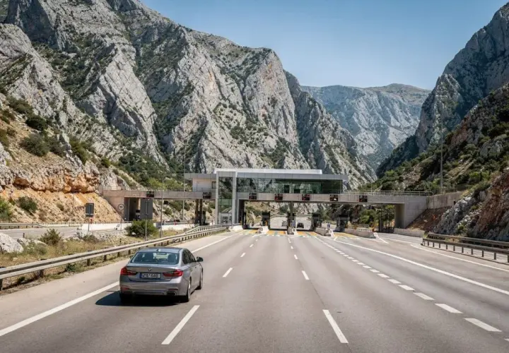Un'auto attraversa un casello autostradale tra montagne rocciose. Calcolare quanto costa andare in Croazia in macchina è fondamentale per pianificare il viaggio.