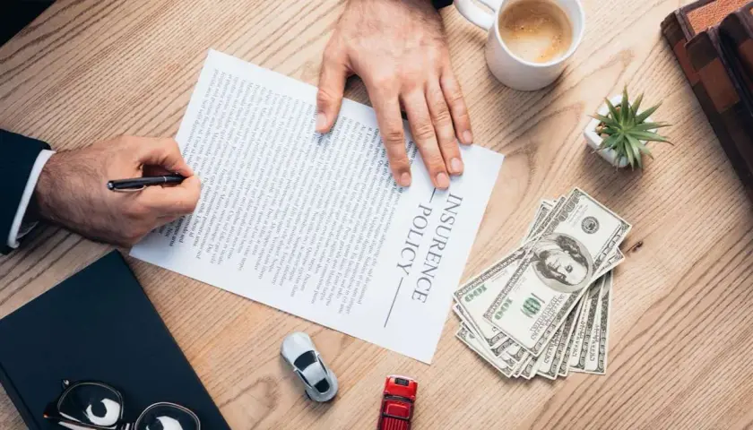 Firma un contratto di assicurazione senza franchigia: cosa significa? Pagamento in contanti, auto e caffè sul tavolo.