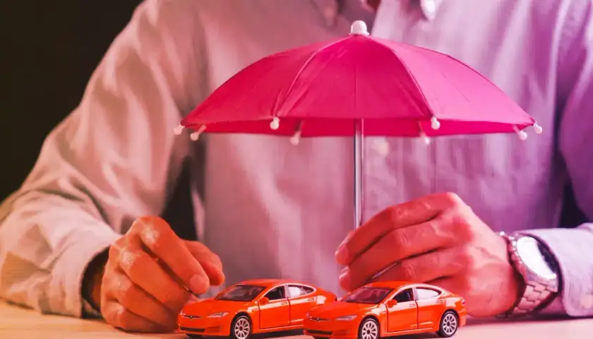 Due macchinine arancioni sotto un ombrello rosa. La protezione è importante, esiste ancora la legge Bersani per assicurare i veicoli.