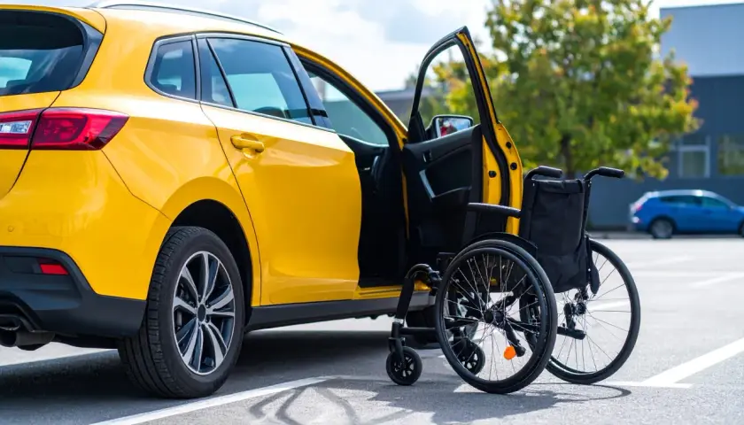Auto gialla con portiera aperta e carrozzina accanto, simbolo di un nuovo inizio e del passaggio di proprietà auto acquistata con legge 104.
