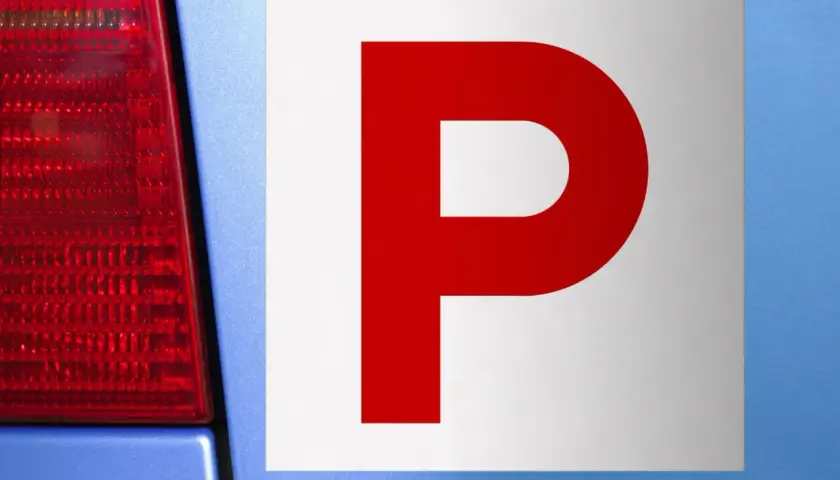 Targa "P" rossa su sfondo bianco, applicata su un'auto blu. Indica un neopatentato alla guida.