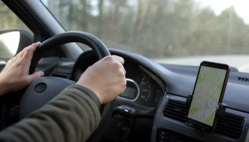 Mani sul volante, un cellulare con mappa mostra la strada. La guida con cellulare è essenziale per orientarsi.