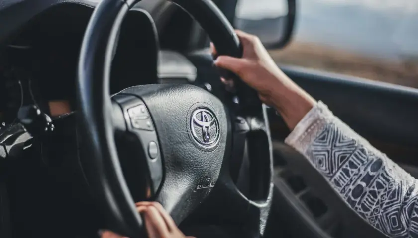 Mani sul volante di una Toyota, con un braccio che indossa una maglia decorata. Finalmente posso guidare una macchina non intestata a me, verso l'avventura.