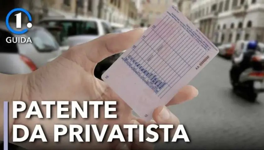 Mano che mostra la patente B, con testo "PATENTE DA PRIVATISTA" e sfondo sfocato di strada con auto e moto.