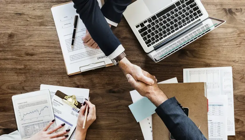 Accordo raggiunto: stretta di mano tra due uomini d'affari, con laptop e documenti. Il contraente significato è chiaro: un patto siglato.