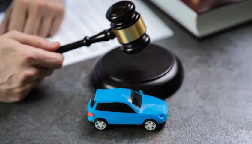 Martelletto da giudice vicino a un'auto blu giocattolo, suggerisce il costo della perdita di possesso in un contesto legale.