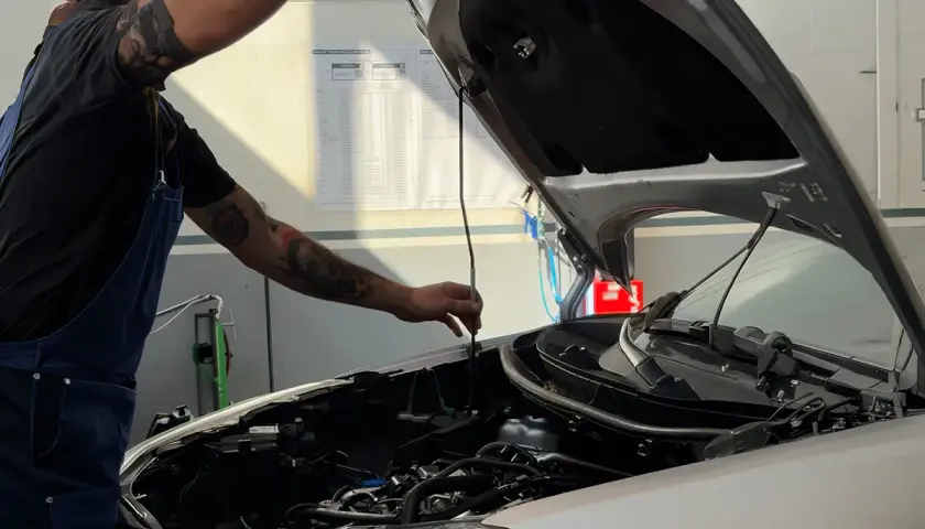 Meccanico con tatuaggi controlla il motore, parte essenziale del tagliando della macchina.