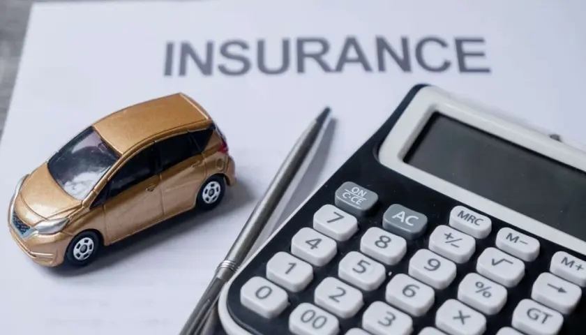 Modellino auto dorata su foglio "INSURANCE", calcolatrice e penna. L'auto intestata al figlio, l'assicurazione al padre.