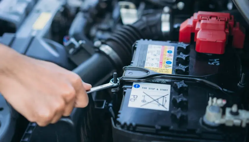 Mano con chiave inglese che allenta il bullone per staccare la batteria auto e non farla scaricare.