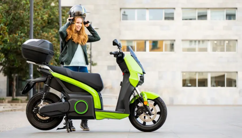 Donna sorridente mette il casco accanto al suo scooter elettrico verde brillante.