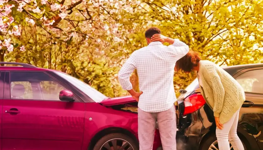 Coppia esamina i danni dopo un incidente. Il cofano di un'auto rossa è aperto, mentre un'altra auto nera è danneggiata. Il **RCA significato** è la copertura assicurativa obbligatoria.