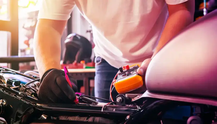 Meccanico con guanti neri effettua il tagliando motorino, usando un multimetro per controllare l'elettronica.